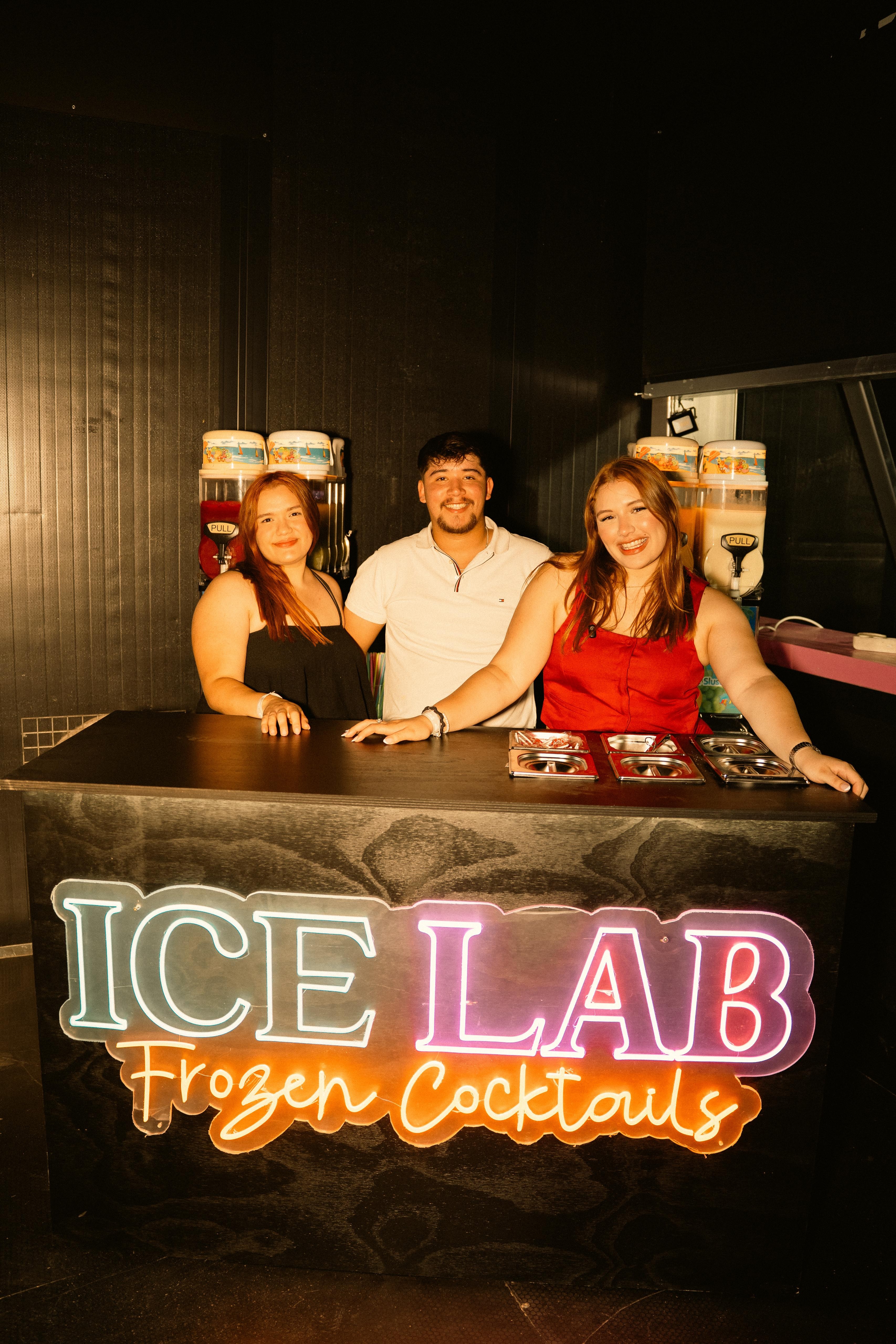 Equipo de ICE LAB con camisetas de marca sosteniendo cócteles granizados en un evento nocturno